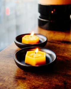 two lit tealight candles on black saucers