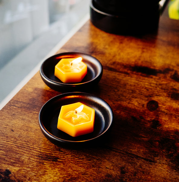 two tealight beeswax candles on black saucer on a wood table