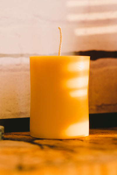 3" by 4" beeswax pillar candle in front of a wall and shadows casted on it